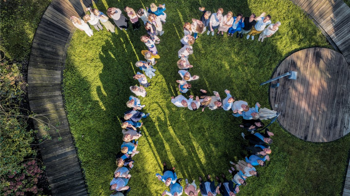 Drohnenaufnahme von Menschengruppe im Garten die eine 75 bilden